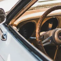 Detaljer från en klassisk bil. Ratt, instrumentbräda och dörrsida i brunt läder. Perfekt för att lära sig hur startar man en manuell bil.