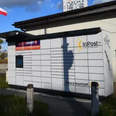 Paczkomat InPost z logo Allegro Smart. W tle polska flaga i budynek. Ile jest paczkomatów w Polsce? Tysiące!
