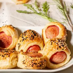 Délicieux feuilleté saucisse, dorés et parsemés de graines de sésame, sur une assiette blanche.
