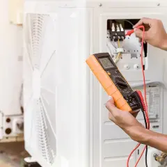 Technik z certyfikatem f-gaz sprawdza klimatyzator multimetrem.