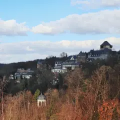 Blick auf Schloss Burg, das majestätisch auf einem Hügel thront, umgeben von Bäumen. Ein kleiner Pavillon im Vordergrund, im winterlichen Wupper Tal.