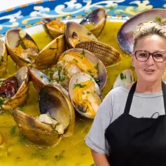 Una mujer sonriente presenta un plato de almejas al ajillo, conchas abiertas en una salsa dorada con perejil picado.
