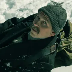 Mężczyzna w czapce i płaszczu leży w śniegu. Jego twarz wyraża zdziwienie. Scena z filmu "Biała odwaga".