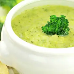 Aksamitna zupa krem z brokułów z ziemniakami, udekorowana różyczką brokułu. Obok kromki chleba.