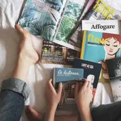 Osoba leży na łóżku otoczona **ciekawymi książkami po angielsku**. Widać fragmenty okładek z ilustracjami i tytułami.