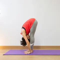 Mujer en postura de Uttanasana yoga, estirando su cuerpo hacia abajo.