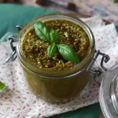 Słoik z pysznym, domowym pesto pistacjowym, ozdobiony listkami bazylii. Idealne do makaronu i kanapek.