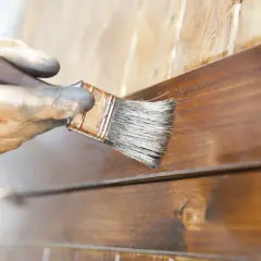Mano enguantada aplica barniz a madera. El proceso de lijar entre capas de barniz asegura un acabado perfecto.