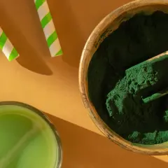 Zielony proszek w drewnianej misce i szklanka napoju. To spirulina – co to jest? Superfood pełen wartości odżywczych.