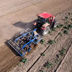 Un tracteur rouge travaille le sol avec un cultivateur, préparant le terrain pour la culture sans labour.