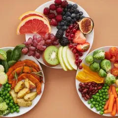 Platos con frutas y verduras frescas, incluyendo arándanos, fresas, uvas, kiwi, brócoli, zanahorias y guisantes. Una selección de alimentos diuréticos para una dieta saludable.