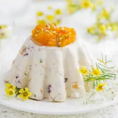 Tradycyjna pascha wielkanocna, udekorowana kandyzowanymi owocami i pistacjami, otoczona wiosennymi kwiatami.