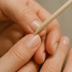 Dłoń z naturalnymi paznokciami i drewnianym patyczkiem do skórek.