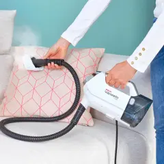 Donna usa un pulitore a vapore per pulire un cuscino sul divano.