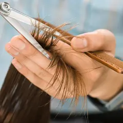 Manos cortando puntas abiertas con tijeras y peine. Pregúntate cada cuanto cortar el pelo para mantenerlo sano.