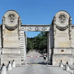 Monumentalna brama cmentarza Père Lachaise z łacińskimi inskrypcjami i płonącymi pochodniami.