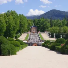 Jardín de la Granja de San Ildefonso, Madrid. Escalera de agua con estatuas y fuentes, rodeada de vegetación y montañas.