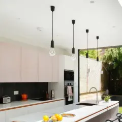 Cocina moderna con gabinetes rosados y una lámpara de barra colgante sobre la isla. Ventanales dan a un jardín exuberante.