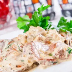 Soczysty schab w sosie koperkowym, udekorowany świeżą natką pietruszki, prezentuje się apetycznie na białym talerzu.