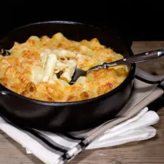 Un plat réconfortant de gratin de pâtes à l'ancienne, doré et gratiné au fromage, servi dans un plat noir avec une cuillère.