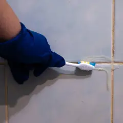 Main bleue, brosse à dents et produit nettoyant pour lutter contre la moisissure joint salle de bain.