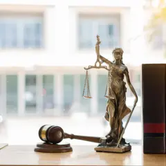Figurka Temidy, symbol sprawiedliwości, obok młotka sędziowskiego i ksiąg. To alegoria co to znaczy dla prawa.