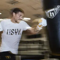 A boxer in a white t-shirt and gloves trains intensely during a boxing training camp, punching a heavy bag.
