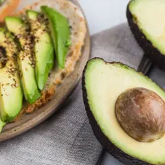 Avocado-Toast mit Gewürzen und frischem Basilikum. Ist Avocado Obst oder Gemüse? Botanisch ist sie eine Frucht, kulinarisch oft als Gemüse verwendet.