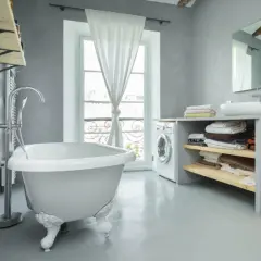 Un baño moderno con bañera independiente, lavadora y estantes con toallas. La idea de pintar bañera aquí es para un estilo minimalista.