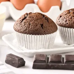 Dos magdalenas de chocolate recién horneadas, listas para disfrutar. A su lado, trozos de chocolate y moldes para hornear.