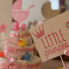 Urocza dekoracja na baby shower z napisem "Little princess", koroną i grzechotką. W tle tort z pieluch i różowa karoca. Prawdziwy mały **gwiazdor**!