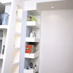 Scaffali moderni in cartongesso, con libri, vasi e soprammobili, creano un angolo lettura accogliente.