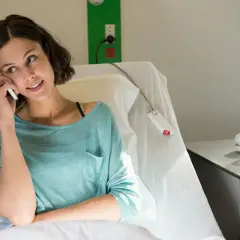 Kobieta w szpitalnym łóżku rozmawia przez telefon, szukając informacji, co niszczy raka.