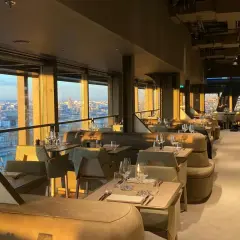 Intérieur d'une brasserie chic avec vue panoramique sur Paris. Les tables sont dressées, prêtes à accueillir les clients pour un dîner inoubliable à la Madame Brasserie Tour Eiffel.