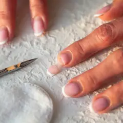 Dłonie z francuskim manicure, nożyczki i wacik. Zastanawiasz się, dlaczego nie rosną paznokcie u rąk? Może to kwestia pielęgnacji.