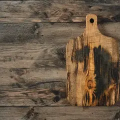 Planche à découper en bois brut, brûlée et texturée, sur un fond de planches de bois vieilles. Idéal pour apprendre comment traiter une planche de bois brut.