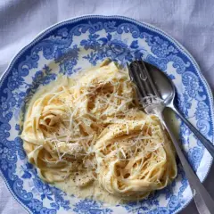 Tagliatelle w kremowym sosie alfredo, posypane parmezanem, na talerzu z niebieskimi wzorami.