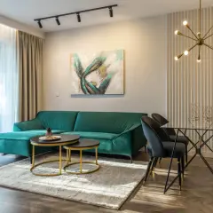 Elegancki salon z kanapą w odcieniu głębokiej zieleni, nowoczesnym stołem i designerską lampą.