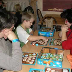 Rodzina gra w planszówkę Super Farmer. Chłopiec przesuwa pionek, a obok leży instrukcja.