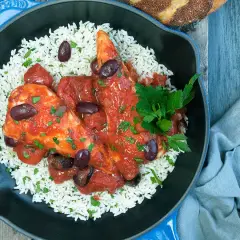 Un plat de poulet sauce tomate savoureux, servi sur un lit de riz blanc, garni d'olives noires et de persil frais.