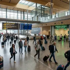 Ludzie z bagażami przechodzą przez nowoczesne lotniska w Norwegii, kierując się do odbioru bagażu lub odprawy celnej.