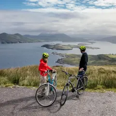 Pareja disfrutando de un paseo en bicicleta por la costa de Irlanda, con vistas a islas y montañas.