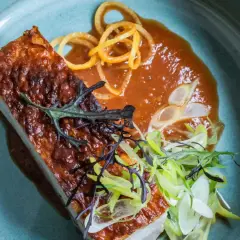 Un morceau de lard croustillant, savamment préparé avec une marinade pour barbecue, servi avec une sauce onctueuse et des garnitures fraîches.