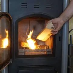 Hand legt Holzscheit mit gutem Brennwert Birke in den brennenden Ofen.