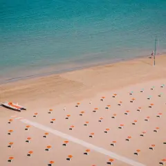 Pusta plaża w Rimini z rzędem pomarańczowych parasoli i małą łodzią motorową.
