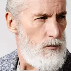 Gros plan sur le visage long d'un homme âgé aux cheveux gris et à la barbe blanche, regardant intensément.