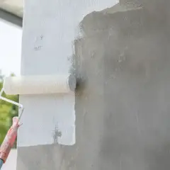 Malowanie betonu wałkiem. Biała farba pokrywa szarą ścianę, odświeżając jej wygląd.