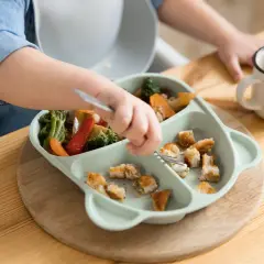 Dziecko je obiad z talerzyka z przegródkami: warzywa i kawałki kurczaka.