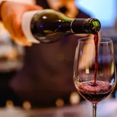 Ciemnoczerwone bordeaux wino leje się z butelki do kieliszka, tworząc piankę.