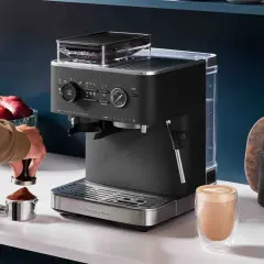 Un uomo prepara il miglior caffè con una macchina KitchenAid. Un bicchiere di cappuccino fumante attende sul bancone.